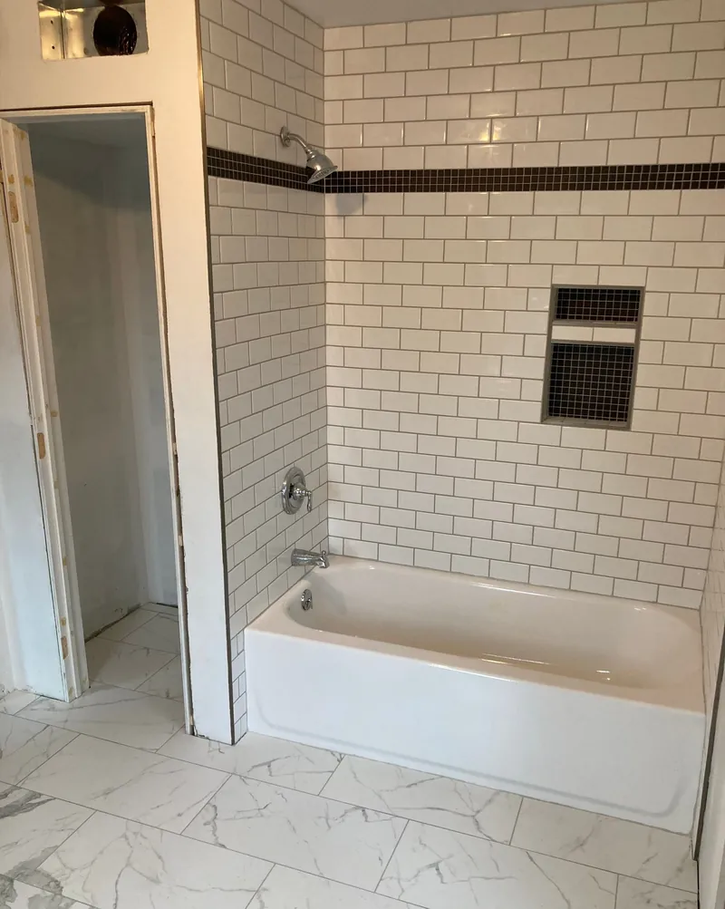 Tub surround in white subway tile with a black mosaic band and niche, in the Harrisburg area.