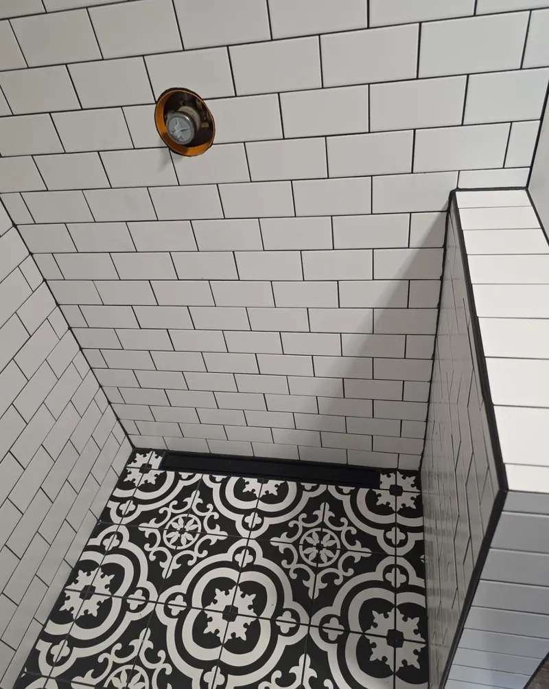 Shower with white subway wall tile and a black and white patterned floor tile.